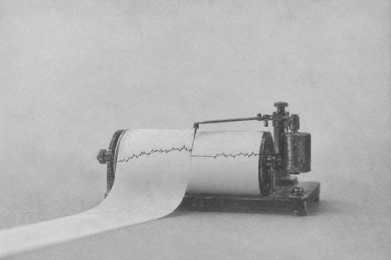 Grainy monochrome illustration of a mechanical recorder tracing an interrupted signal on a paper roll.